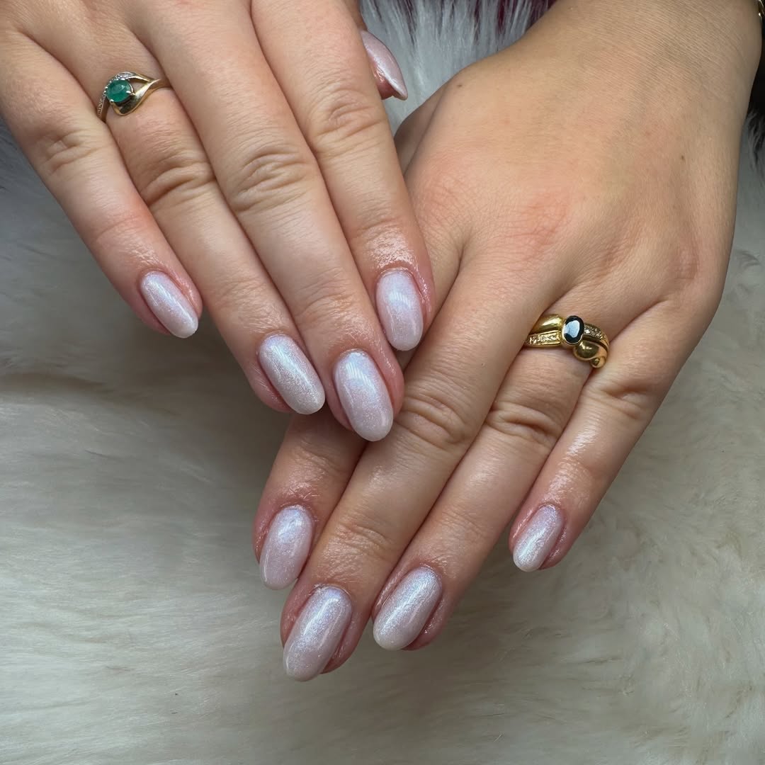 Manucure soignée avec vernis nacré blanc et bagues élégantes sur fond de fausse fourrure.